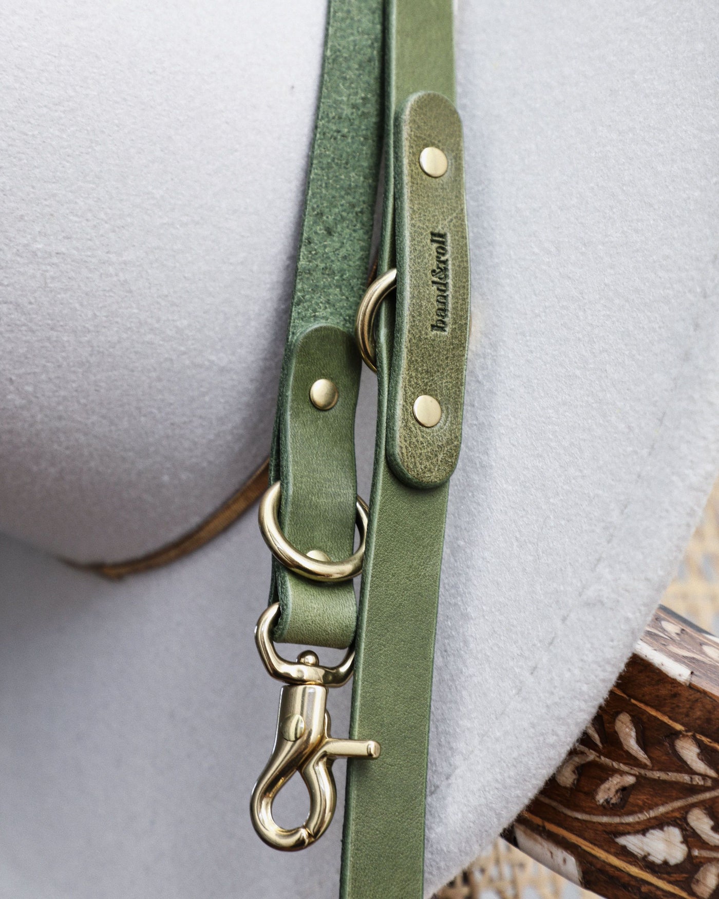 Closeup of green leather crossbody dog leash hanging off hat on chair