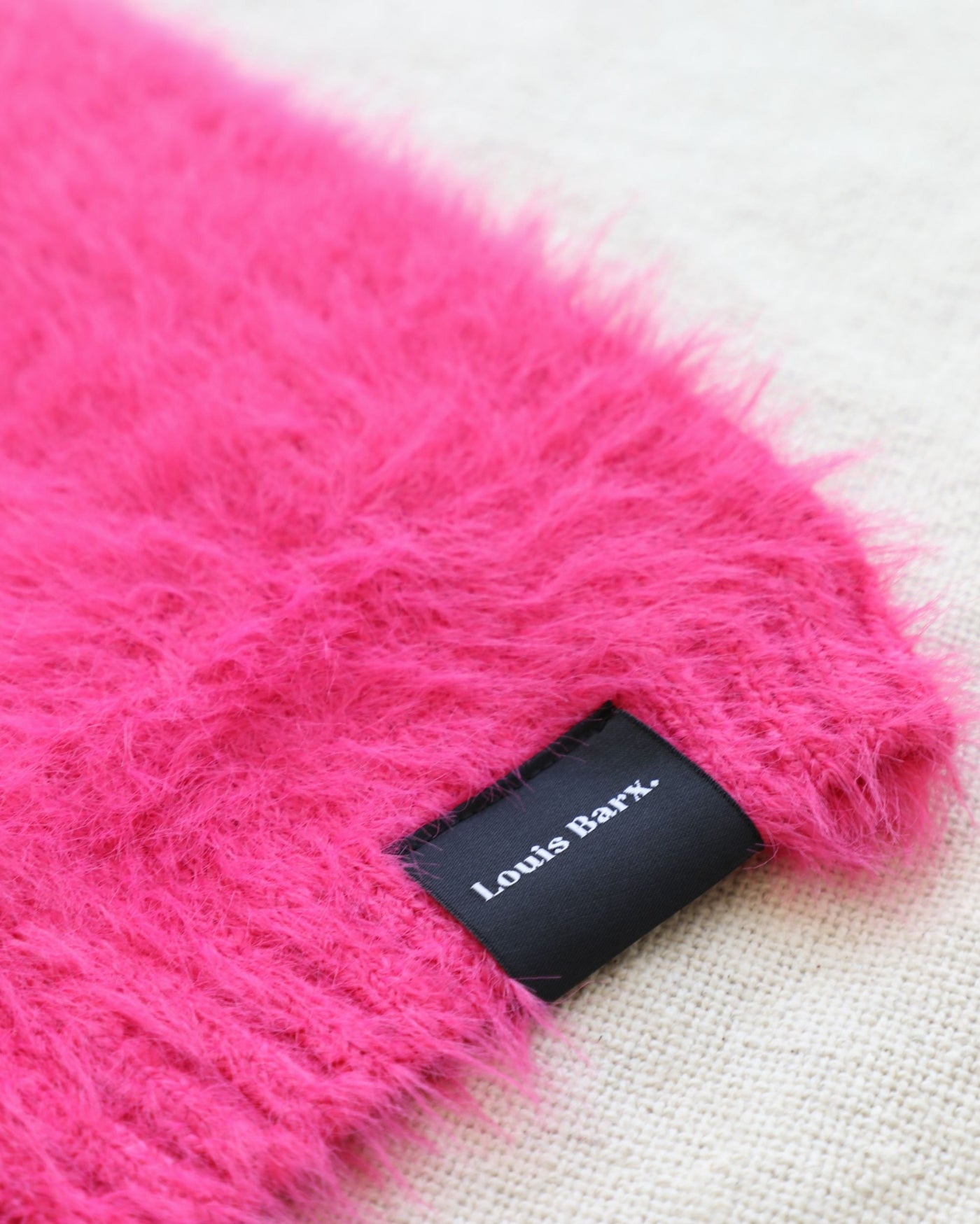 Fluffy hot pink dog sweater on white background, close up of brand tag Louis Barx