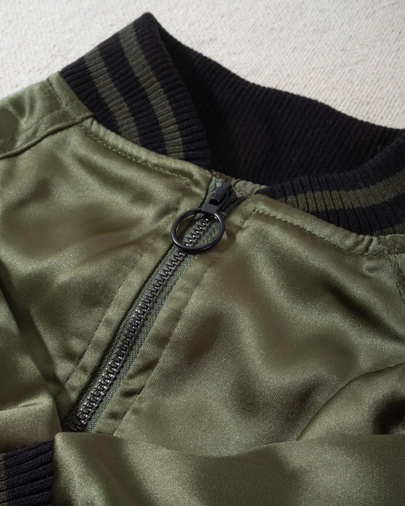 A modern take on a retro classic. Buttery-soft olive green satin practically melts over your pup, with ribbed cuffs and hem, detailed with coordinating green and black stripes. Accented with a chic pewter O-ring pull. 