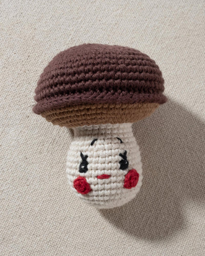 brown and ivory hand knit crochet mushroom dog toy with a smiley face and rosy cheeks