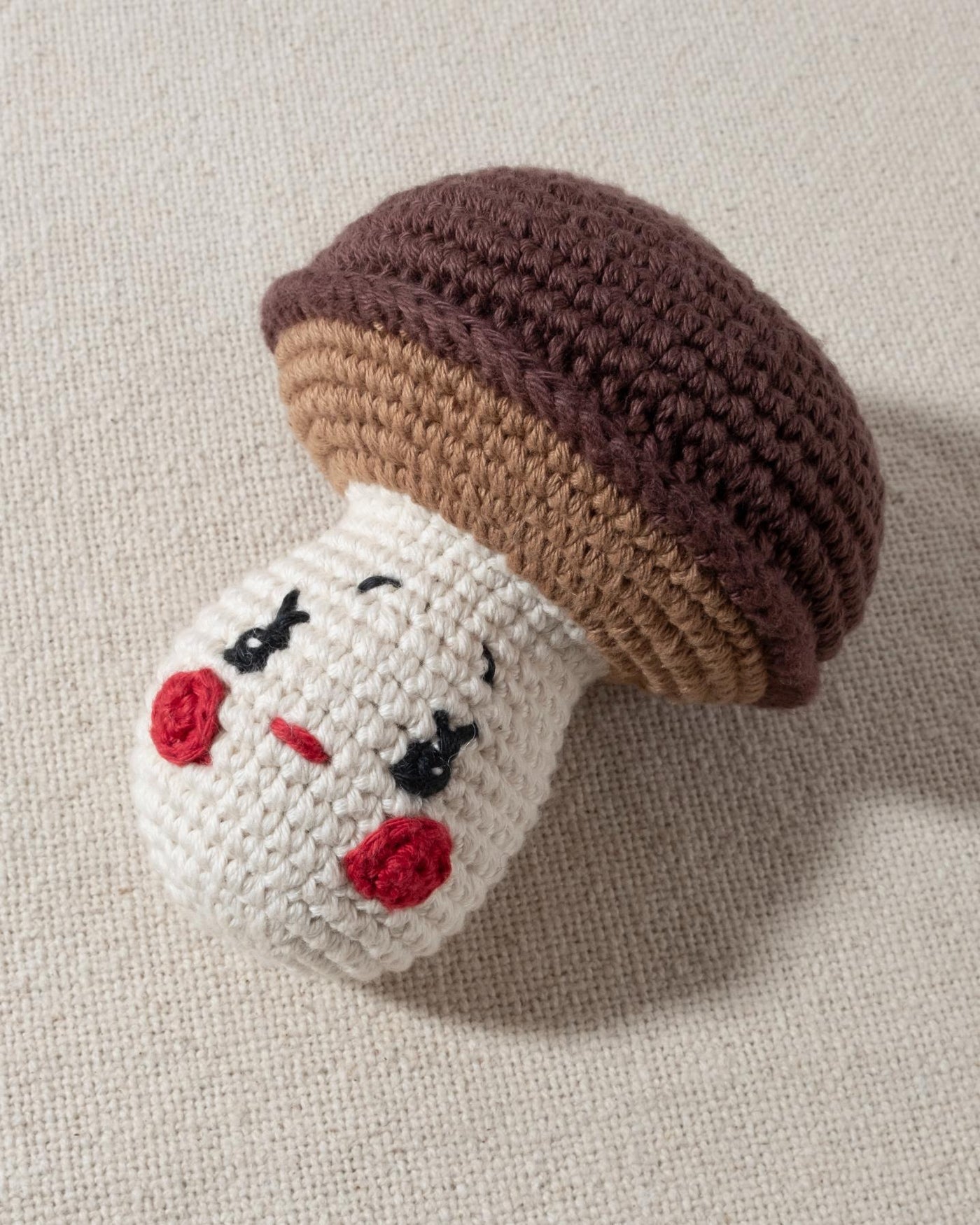 brown and ivory hand knit crochet mushroom dog toy with a smiley face and rosy cheeks