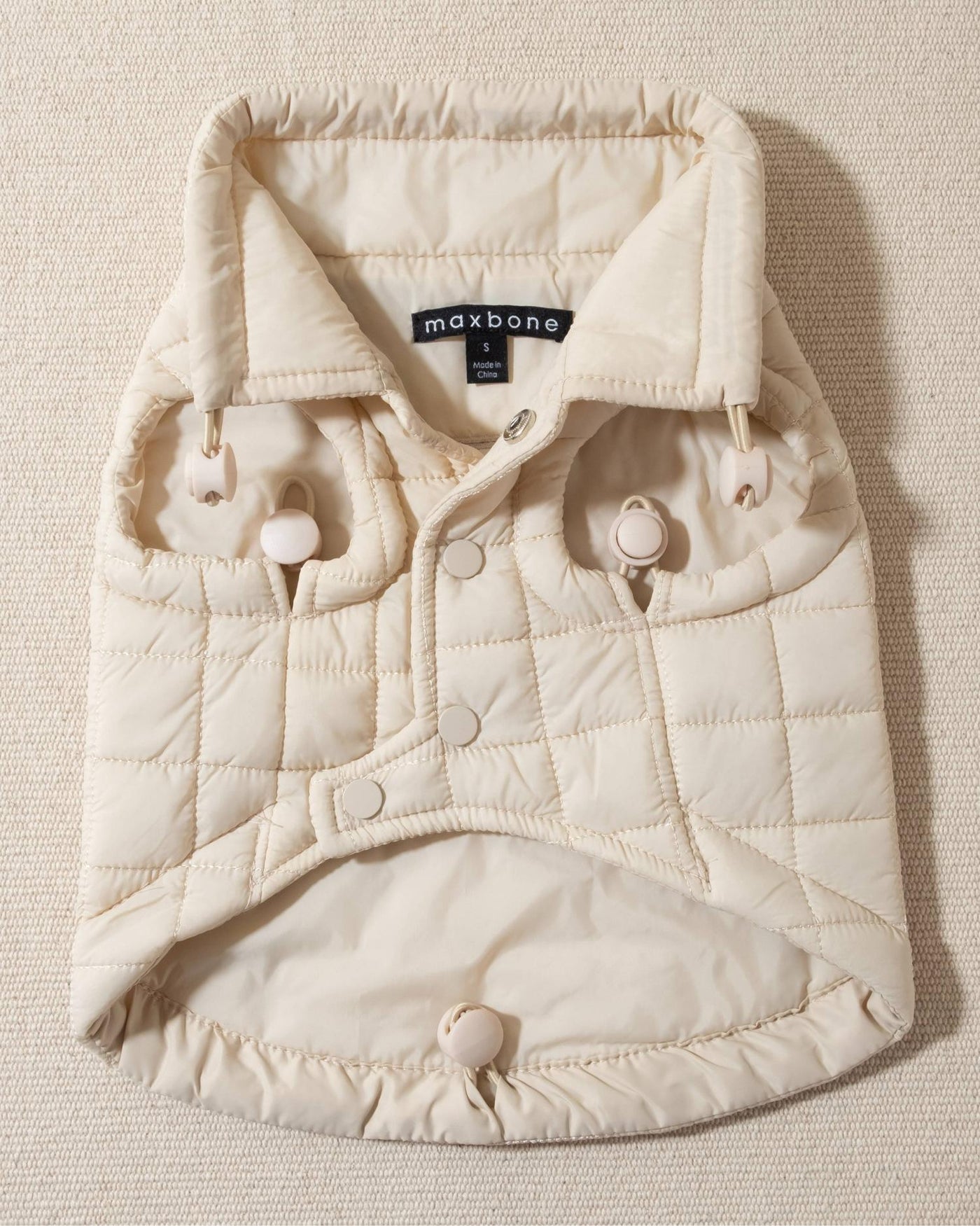 perfect on its own or layered with a cute sweater. This quilted, stylish jacket is fully adjustable, with coordinating sand cords on the hem, neck, and arm openings. Jacket can be worn over harness, with a small opening for leash attachment on the back. Asymmetrical buttons also make for more secure wear, for even the most portly of pups!