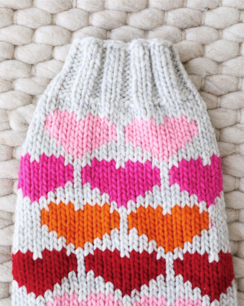 Small dog wearing red knit sweater adorned with white hearts.