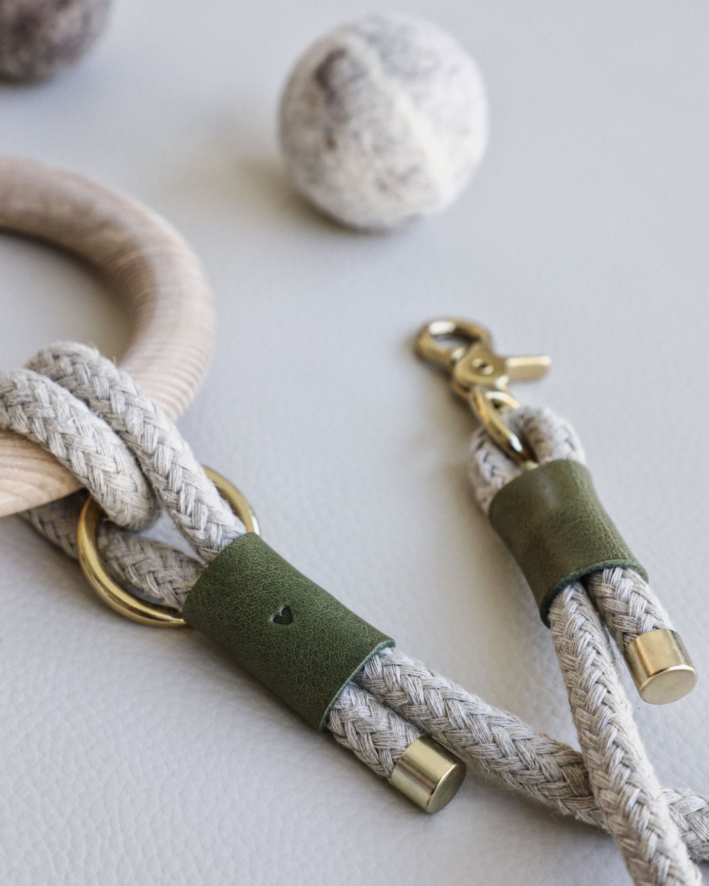Rope leash connected to round dowel with green leather accents and gold hardware. close up of embossed heart in green leather
