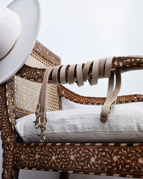 Taupe leather crossbody dog leash hanging off hat on chair