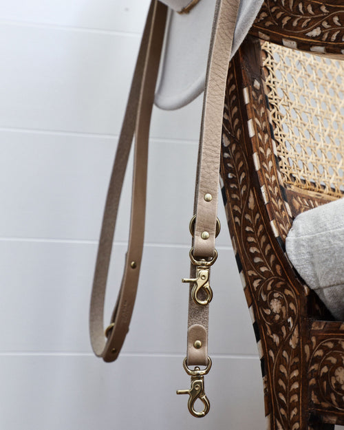 Taupe leather crossbody dog leash hanging off hat on chair