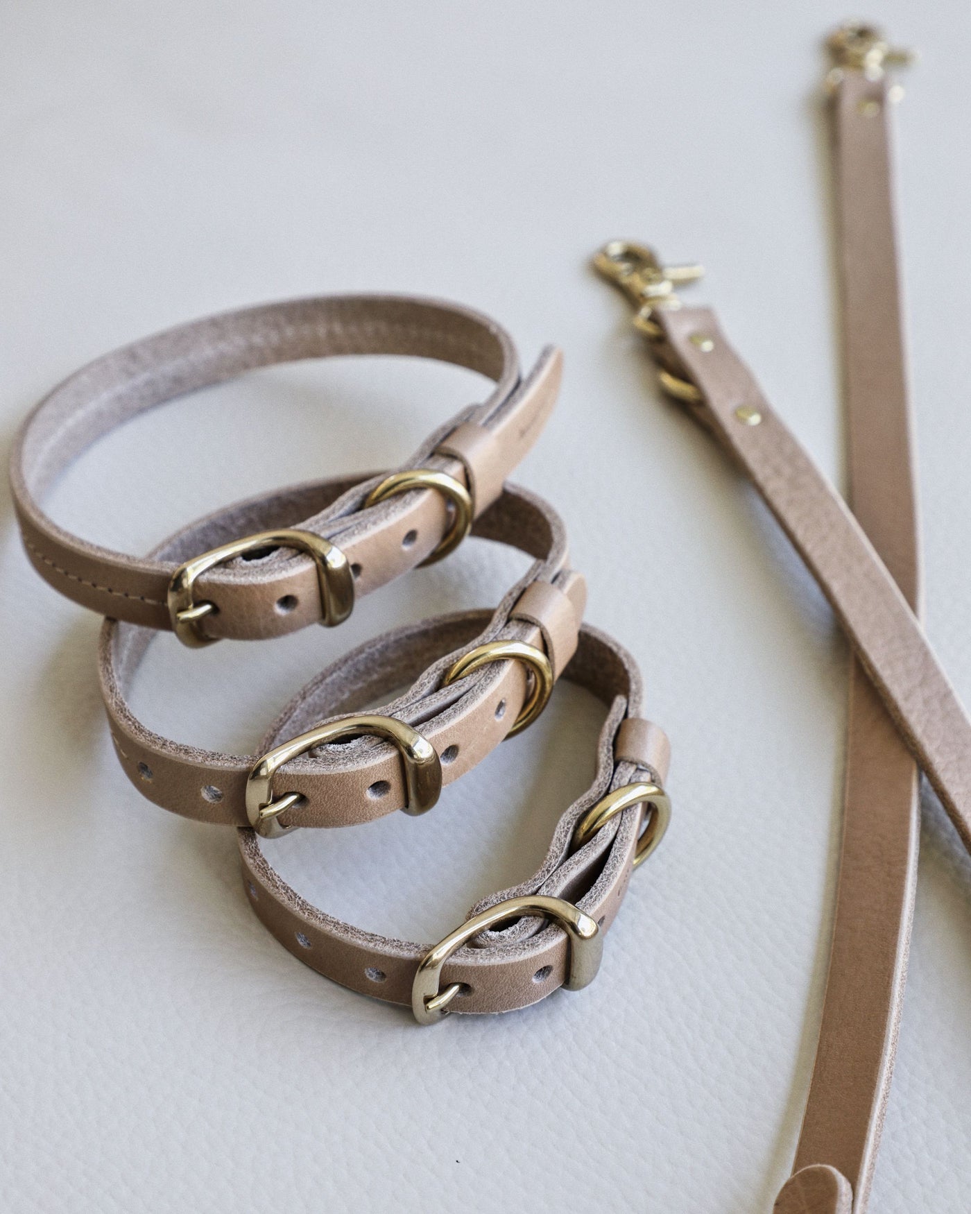 stack of three taupe leather dog collars next to matching taupe leather dog leash