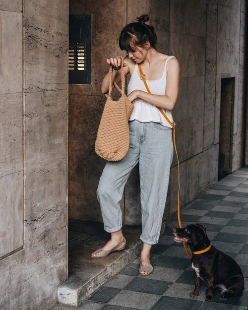 Closeup of green leather crossbody dog leash hanging off hat on chair
