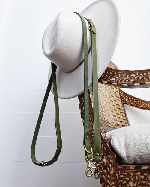 Green leather crossbody dog leash hanging off hat on chair