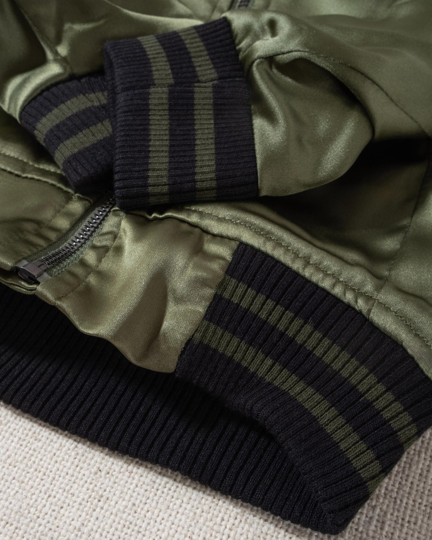 A modern take on a retro classic. Buttery-soft olive green satin practically melts over your pup, with ribbed cuffs and hem, detailed with coordinating green and black stripes. Accented with a chic pewter O-ring pull. 