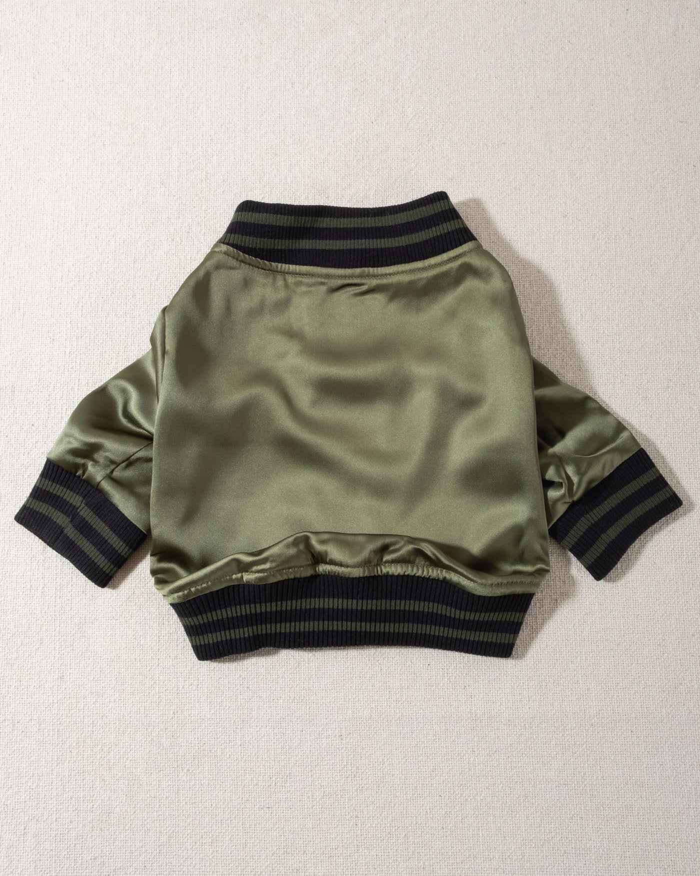 A modern take on a retro classic. Buttery-soft olive green satin practically melts over your pup, with ribbed cuffs and hem, detailed with coordinating green and black stripes. Accented with a chic pewter O-ring pull. 