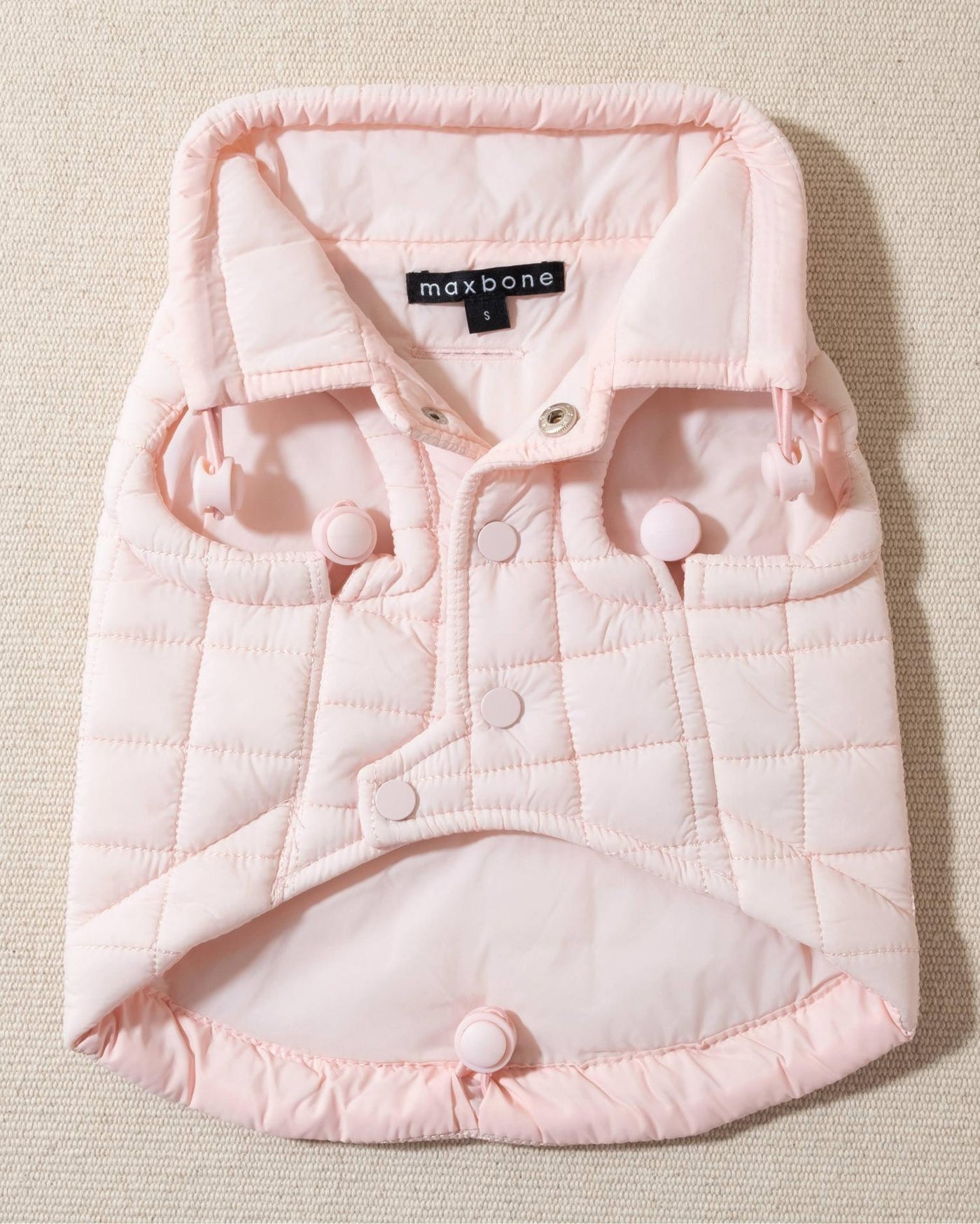 perfect on its own or layered with a cute sweater. This quilted, stylish jacket is fully adjustable, with coordinating light pink cords on the hem, neck, and arm openings. Jacket can be worn over harness, with a small opening for leash attachment on the back. Asymmetrical buttons also make for more secure wear, for even the most portly of pups!